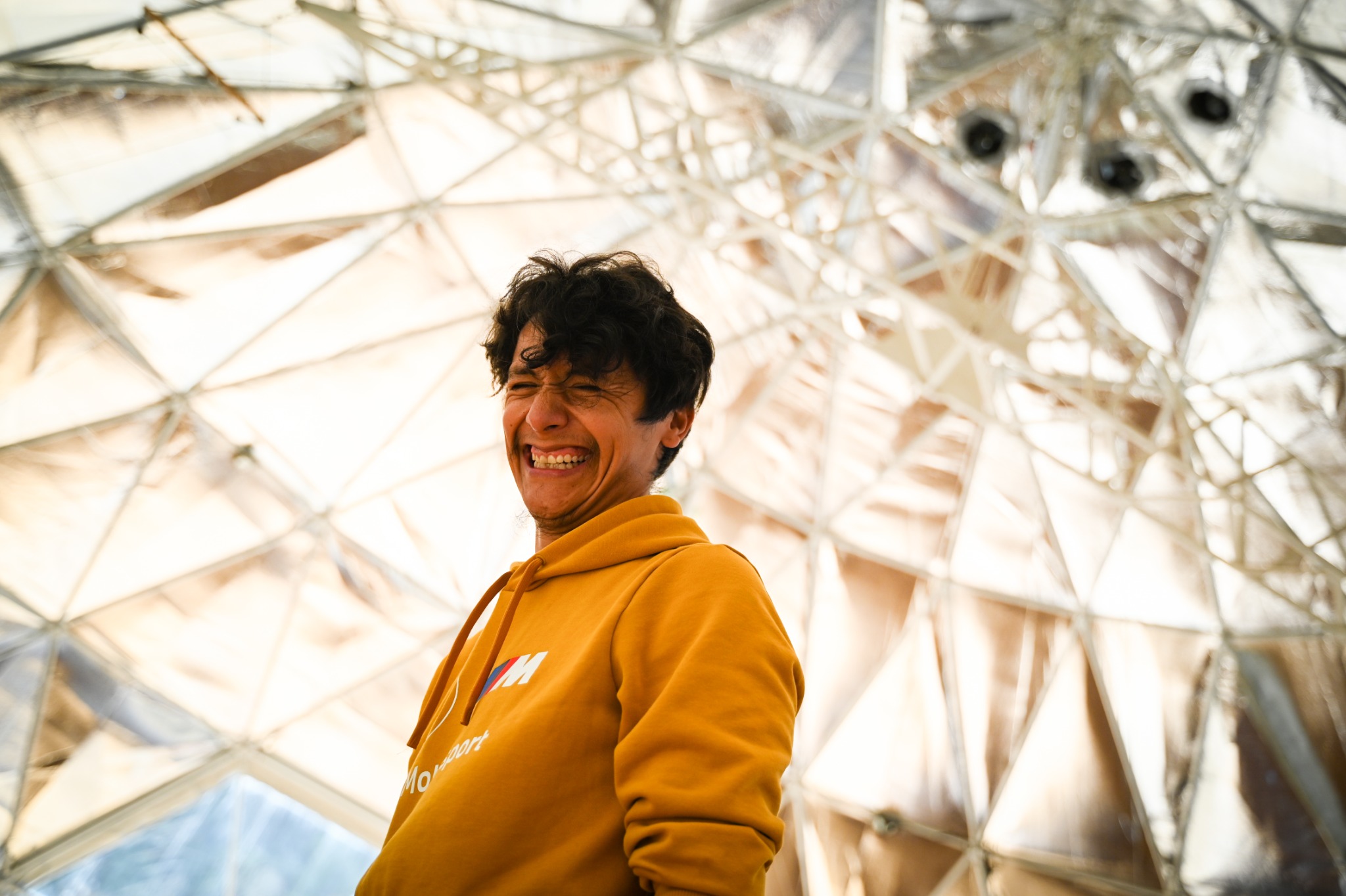 Pablo smiling in a yellow hoodie beneath a geometric dome
